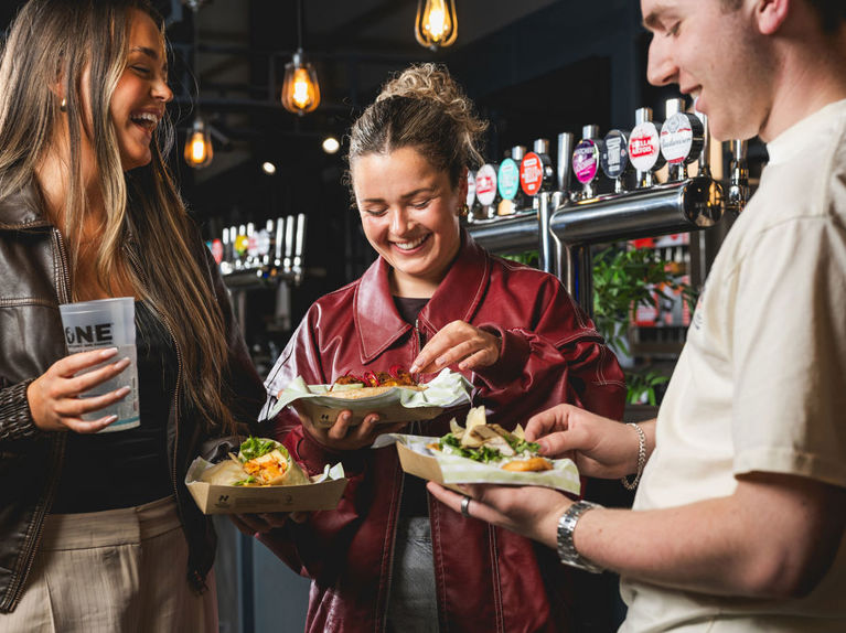 Guests smiling and holding food in a bar venue